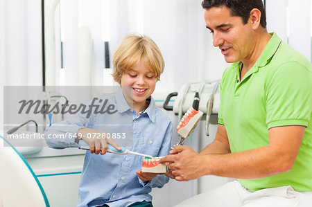 Dentist teaching boy how to brush teeth