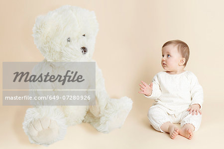 Studio portrait of baby girl next to giant teddy bear