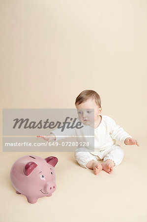 Studio portrait of baby girl reaching for piggy bank