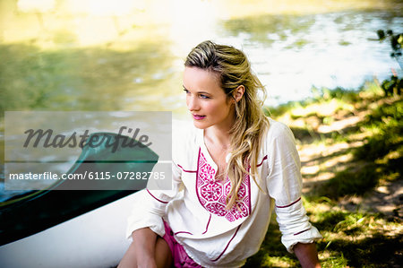 Young woman sits on the riverside, foothills of the Alps, Bavaria, Germany