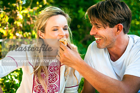 Young man feeding girlfriend on the riverside, foothills of the Alps, Bavaria, Germany