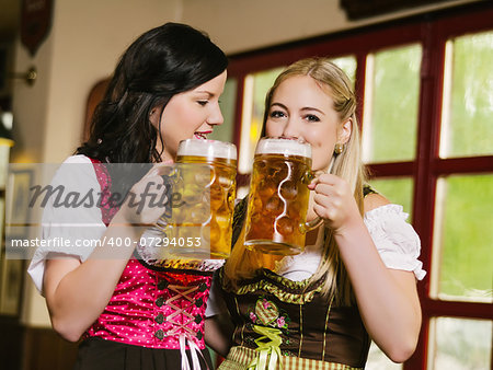 Photo of two beautiful woman wearing traditional dirndl and drinking beer.