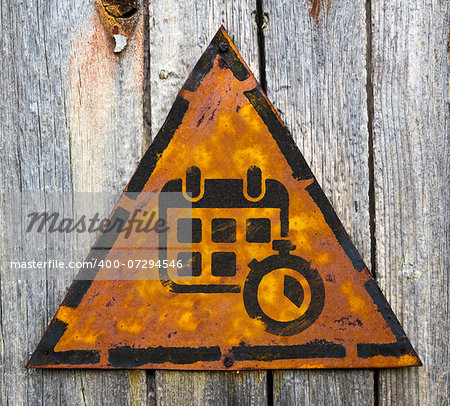 Calendar with Stopwatch Icon on Weathered Triangular Yellow Warning Sign. Grange Background.