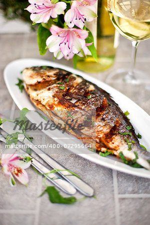 Baked sea bream and glass of white wine on the table