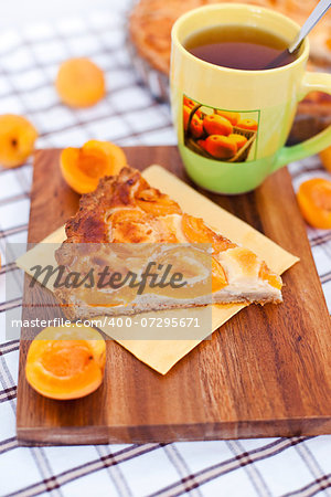 Piece of apricot tart on the wooden board with cup of tea and fresh apricots around