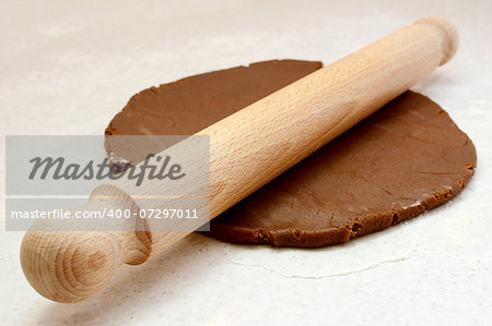 Wooden rolling pin being used to roll out gingerbread cookie dough