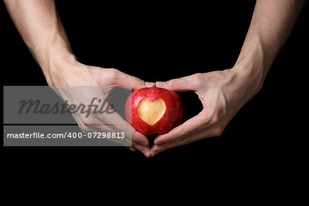 adult man hands holding apple with carved heart, isolated on black