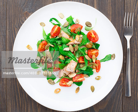 Salad with arugula, salmon, cherry tomato and pumpkin seeds on a plate