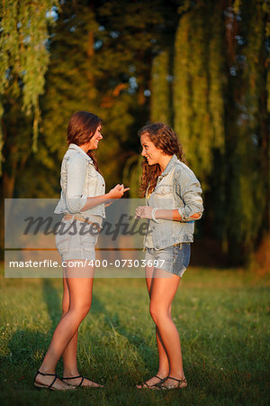 two teenage girls outdoors in jeans wear talking looking at each other