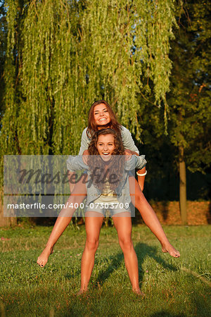 teenage girl giving her girlfriend piggyback ride in park