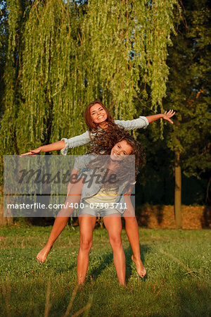 teenage girl giving her girlfriend piggyback ride in park