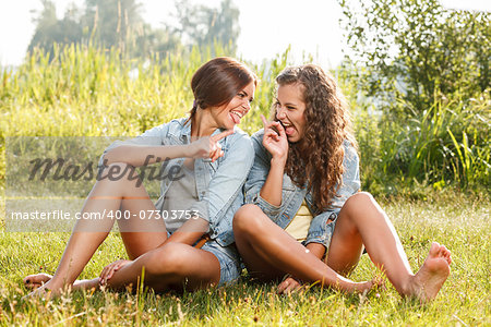 two girlfriends in jeans wear sitting on grass having fun