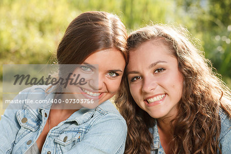 close-up portrait of two girlfriends in jeans wear outdoors sitting  smiling looking at camera