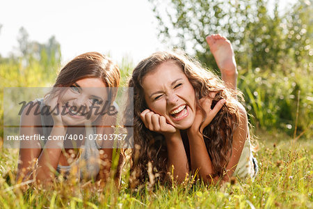 two girlfriends in T-shirts  lying down on grass laughing having good time