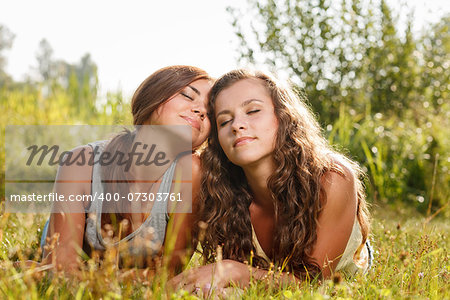 two girlfriends in T-shirts  lying down on grass with eyes closed enjoying each other
