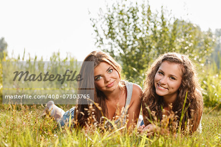 two girlfriends in T-shirts  lying down on grass looking at camera