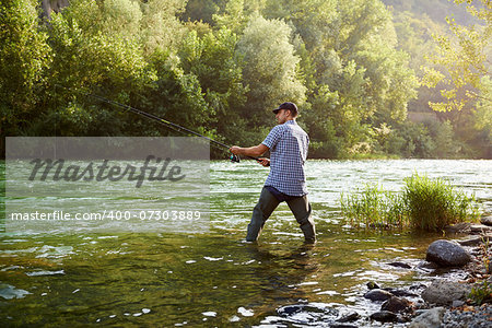 mid adult man on holidays on river, relaxing and fishing trout
