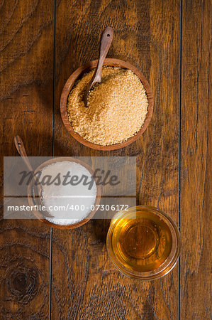 Cane and white sugar in wooden bowls with a spoons.  There is also a glass bowl filled with honey.