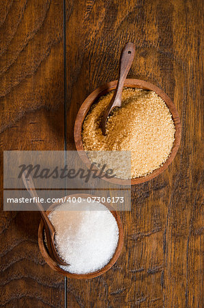 Cane and white sugar in wooden bowls with a spoons.