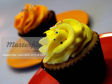 Two Iced Lemon And Orange Cupcakes On Red Plate