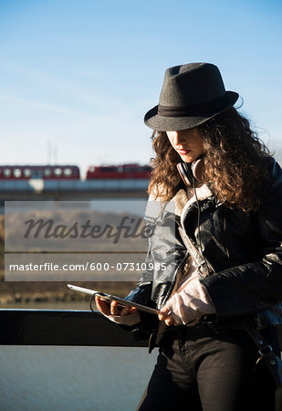 Teenage girl standing outdoors, wearing fedora and using tablet computer, Germany