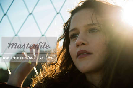 Close-up portrait of teenage girl standing next to chain link fence outdoors, looking into the distance, Germany