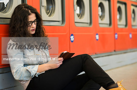 Teenage girl sitting on floor next to dryers, in laundromat, Germany