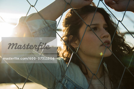 Close-up portrait of teenage girl standing outdoors next to chain link fence, Germany