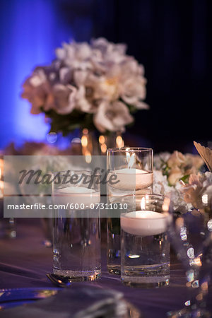 Close-up of floating candles in glass candle holders on table at reception, with flower arrangements in background, Canada