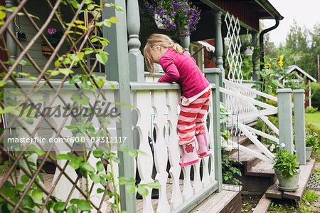 3 year old girl in rubber boots climbing on veranda, Sweden