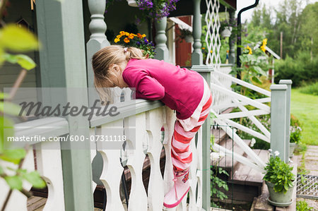 3 year old girl in rubber boots climbs on veranda, Sweden