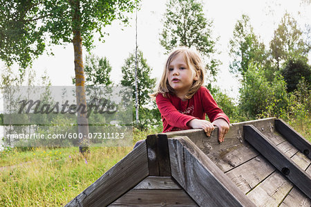 3 year old girl in red shirt climbing on a wooden shed, Sweden