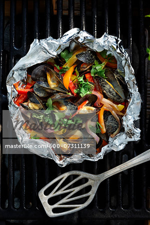 Fresh mussels cooked with yellow peppers, red peppers, orange peppers, red onions and cilantro in a cream sauce in tinfoil on a barbeque grill.