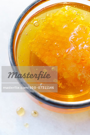 Close-up, overhead view of clear golden honey in a glass with a honey comb and air bubbles