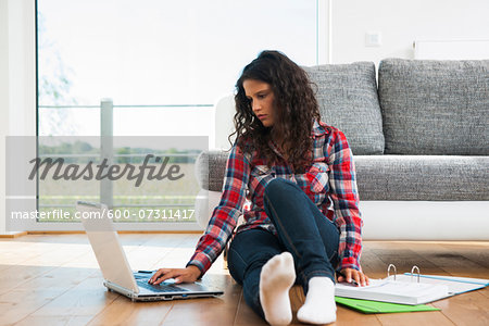 Teenage girl sitting on floor next to sofa, using laptop computer, Germany