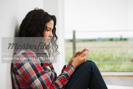 Close-up of teenage girl sitting next to window and using cell phone, Germany