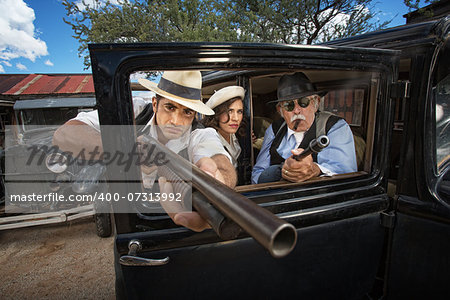 Three 1920s vintage gangsters outside aiming weapons through a window