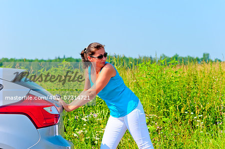 Young beautiful woman is pushing broken car on the road