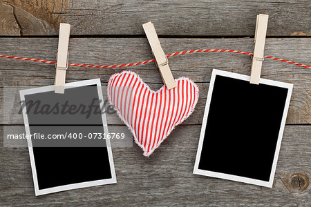 Two blank instant photos and red heart hanging. On wooden background