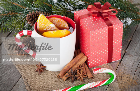 Christmas mulled wine with spices, gift box and snowy fir tree on wooden table