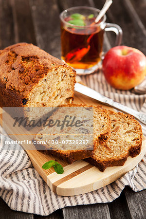 Apple nut cake on wooden board with cup of tea on the background