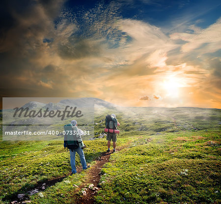 Backpackers on footpath in mountains at sunny day