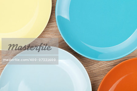 Colorful plates and saucers over wooden table background. View from above