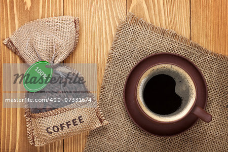 Coffee cup and small bag with beans on wooden table. View from above