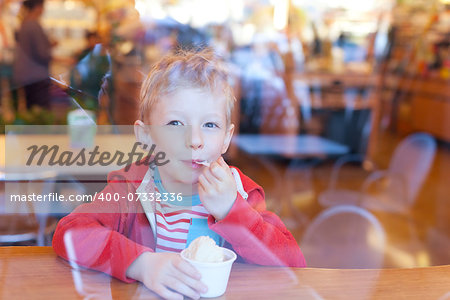 cute little boy enjoying ice cream in cafe, view from outside