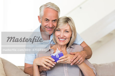 Portrait of a smiling mature man surprising woman with a gift on sofa at home