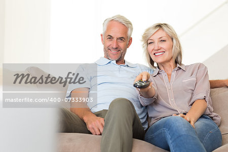 Happy mature couple watching tv on sofa at home