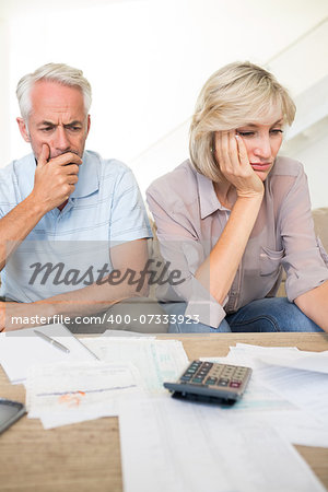 Tensed mature man and woman with bills and calculator sitting on sofa at home