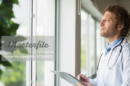 Thoughtful male doctor with clipboard in hospital