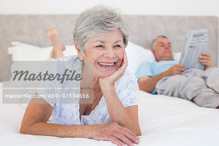 Thoughtful senior woman with man reading newspaper on bed at home